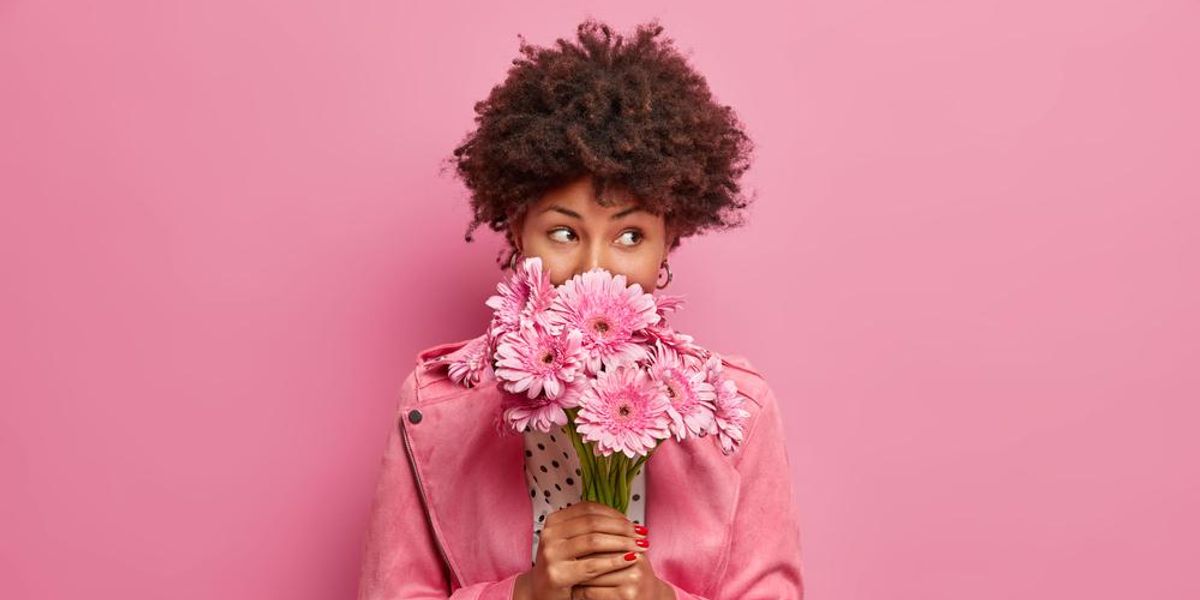 Fiatal nő a kezében tartott virágokat szagolja, rózsaszín háttér előtt