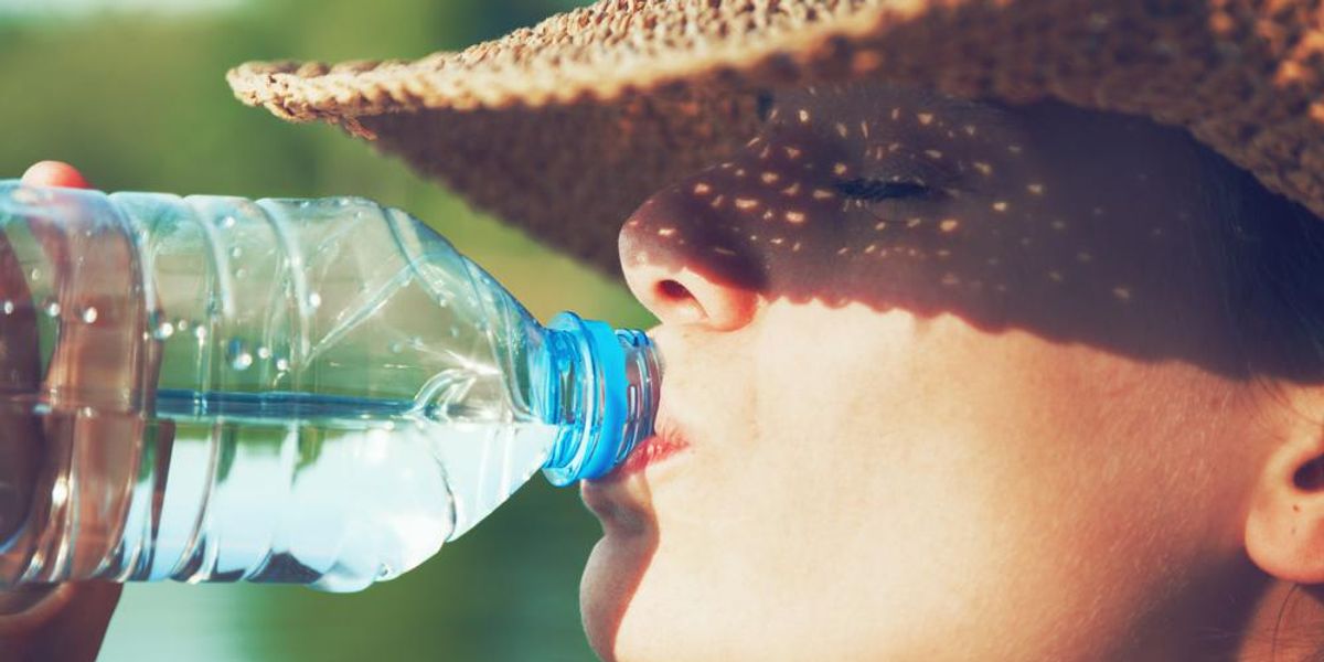 Szalmakalpot viselő nő vizet iszik nyári napfényben