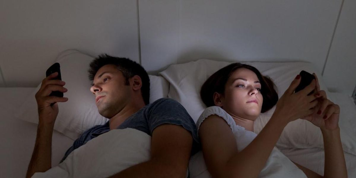 Egy pár tagjai egymás mellett fekve a telefonjukat nyomkodják