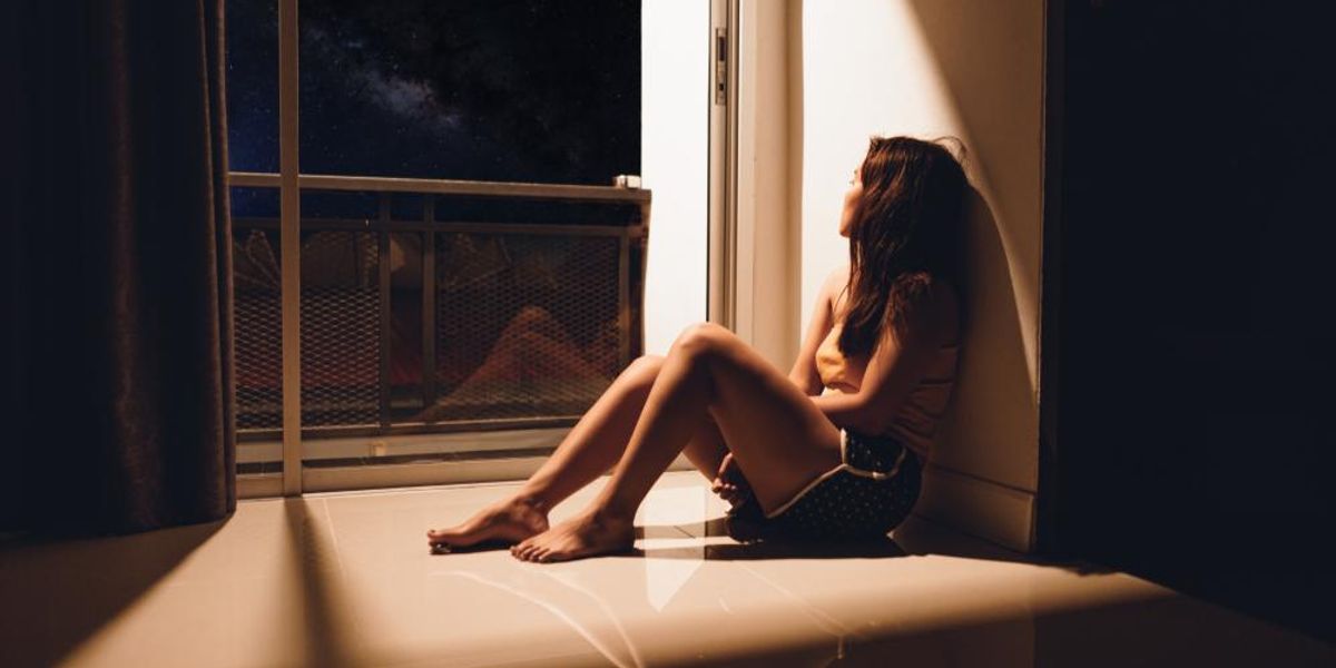 Egy lány egyedül ül az ablaka előtt