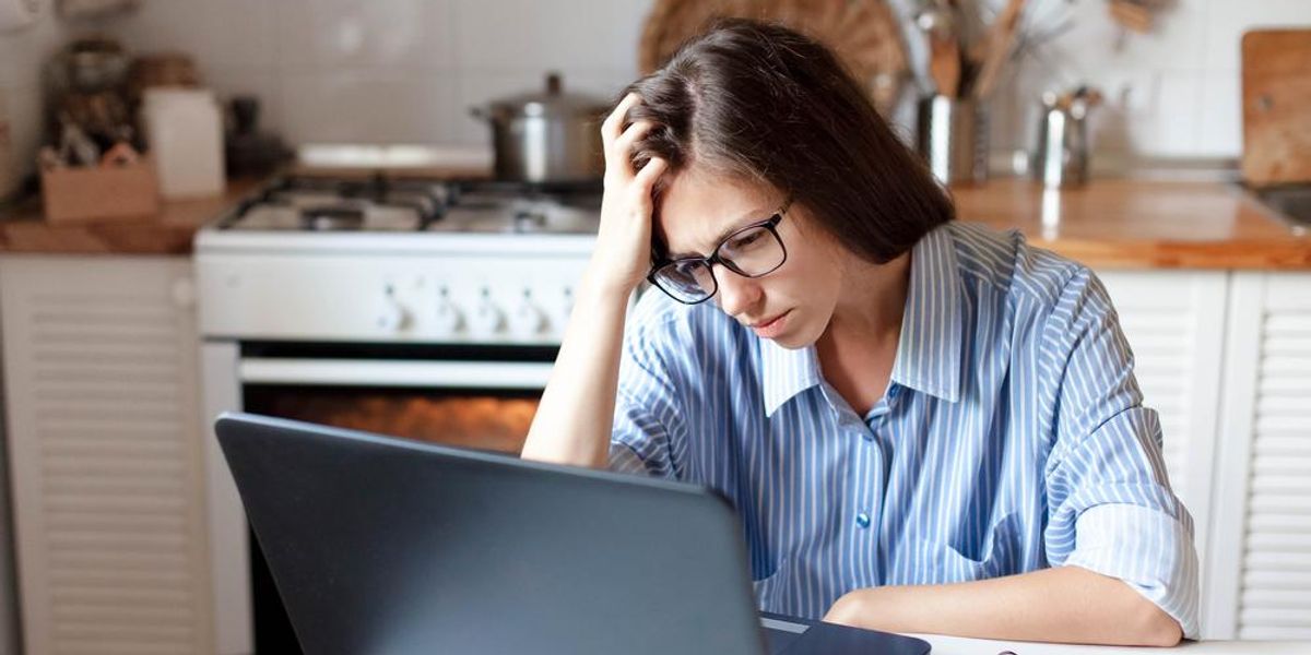 Otthonában dolgozó nő fáradtan nézi a laptopját