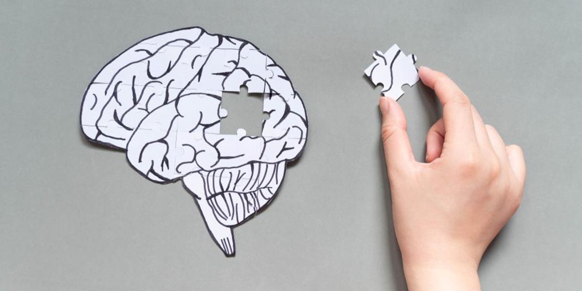 Női kéz próbál az emberi agyat formázó papírforma hiányzó puzzle darabját tartja