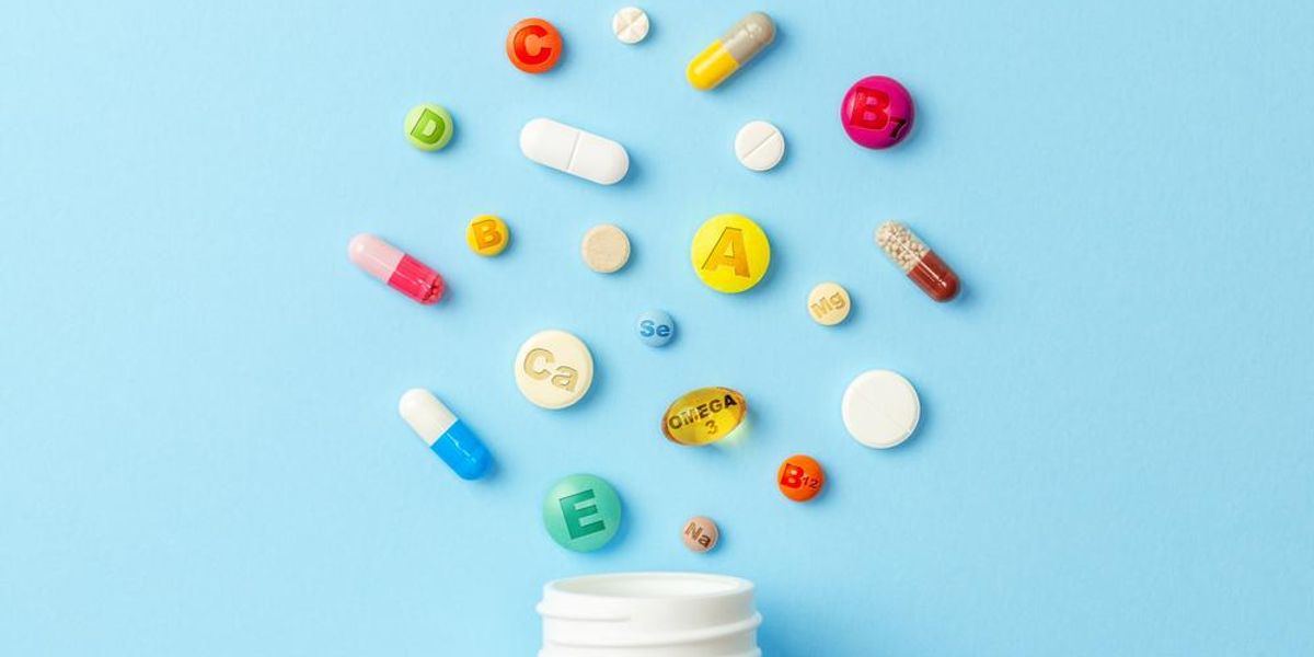 Fehér gyógyszeres doboz, felette színes (multi)vitaminok és tabletták, kék háttéren