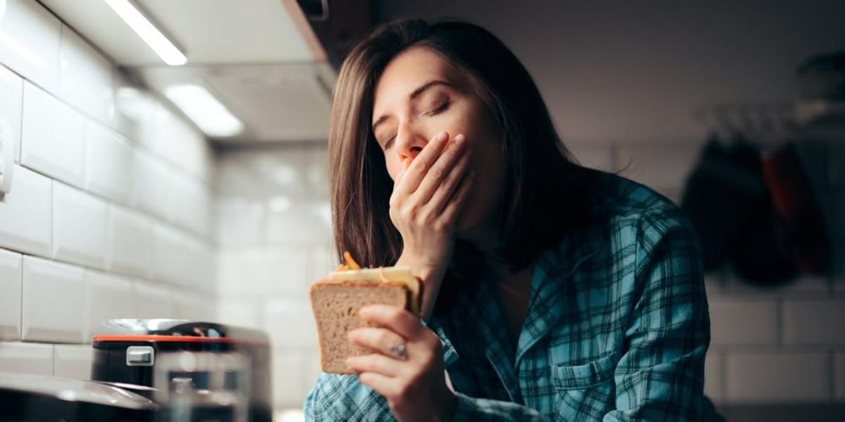 Egy nő éjszaka szendvicset eszik a konyhájában