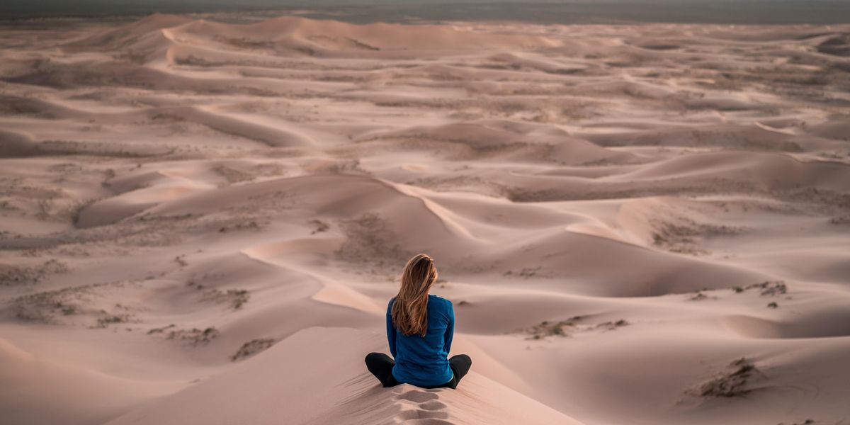 Egy lány egy homokdűnén ül a sivatag közepén
