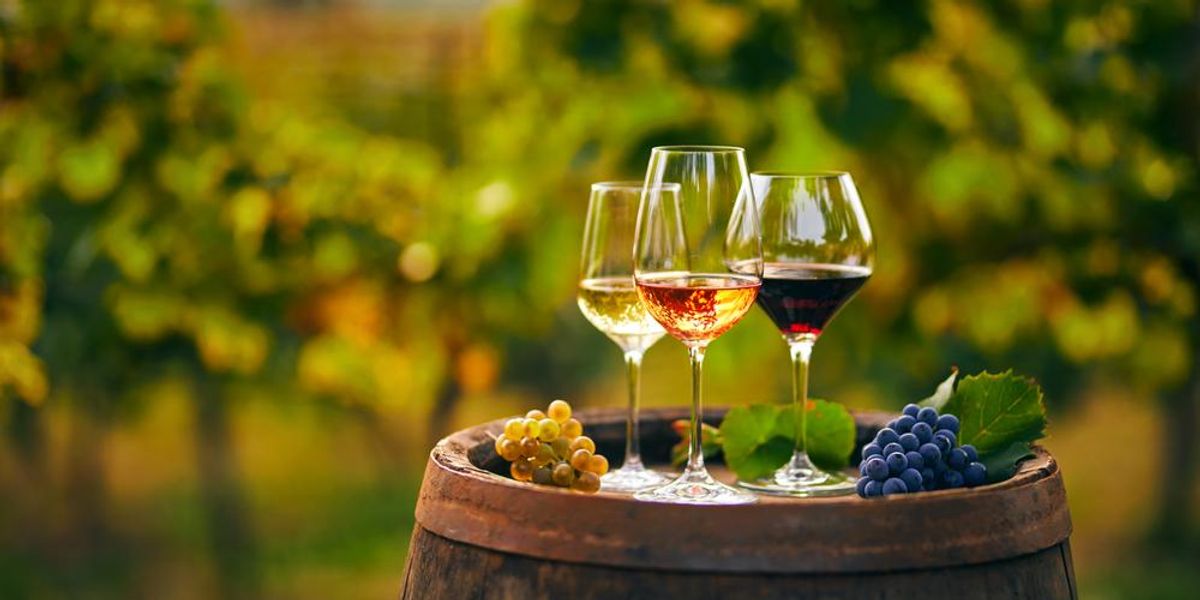 Egy pohár fehér, rozé és vörösbor egy fából készült hordón a szőlősben