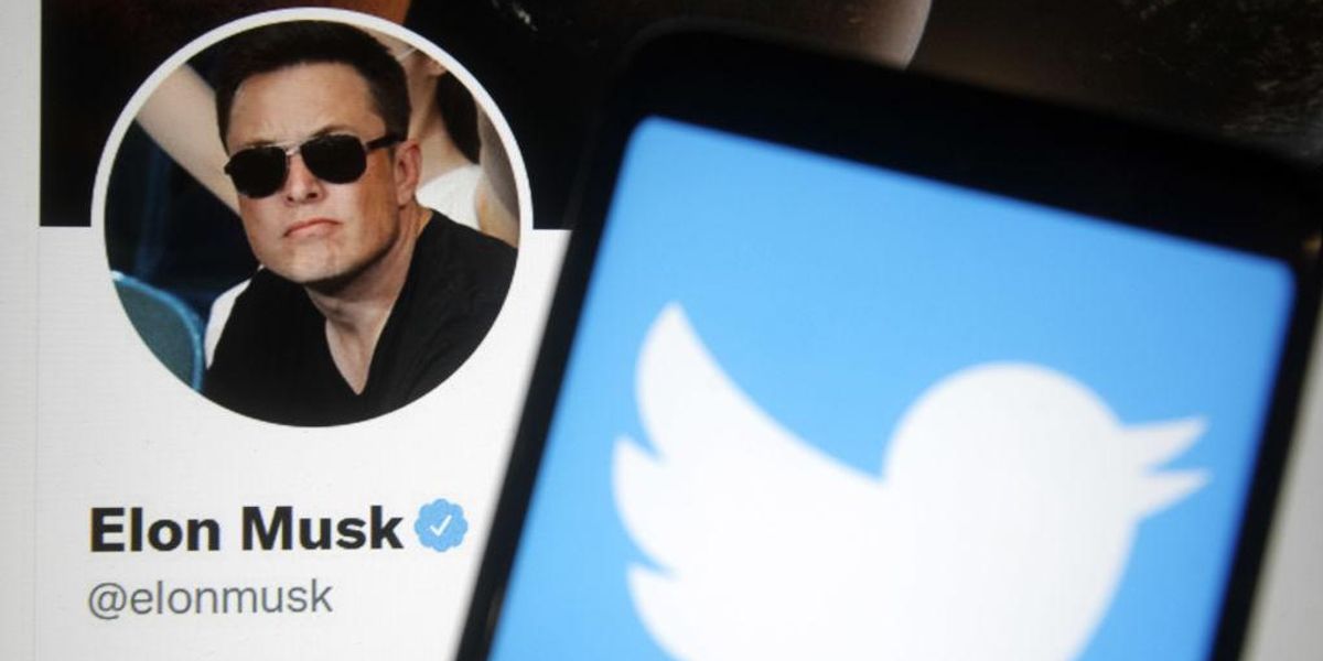 A Twitter logója egy okostelefon képernyőjén, a háttérben pedig Elon Musk Twitter weboldala