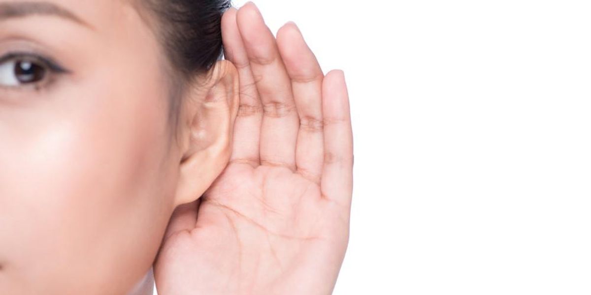 Egy lány a kezét a füléhez tartja, hogy jobban halljon