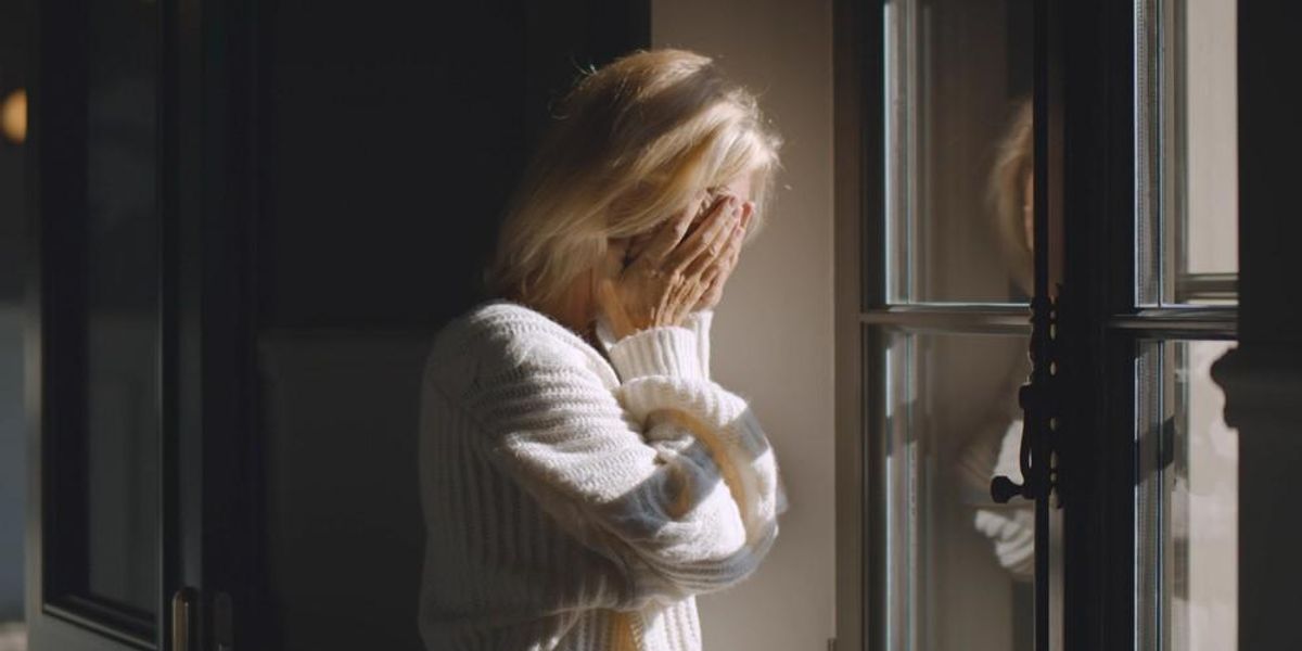Egy nő az ablaka előtt szomorúan takarja az arcát