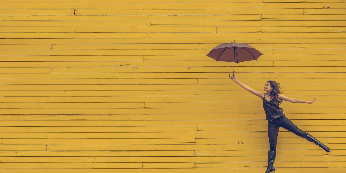 Egy lány esernyővel a kezében egy sárga háttér előtt