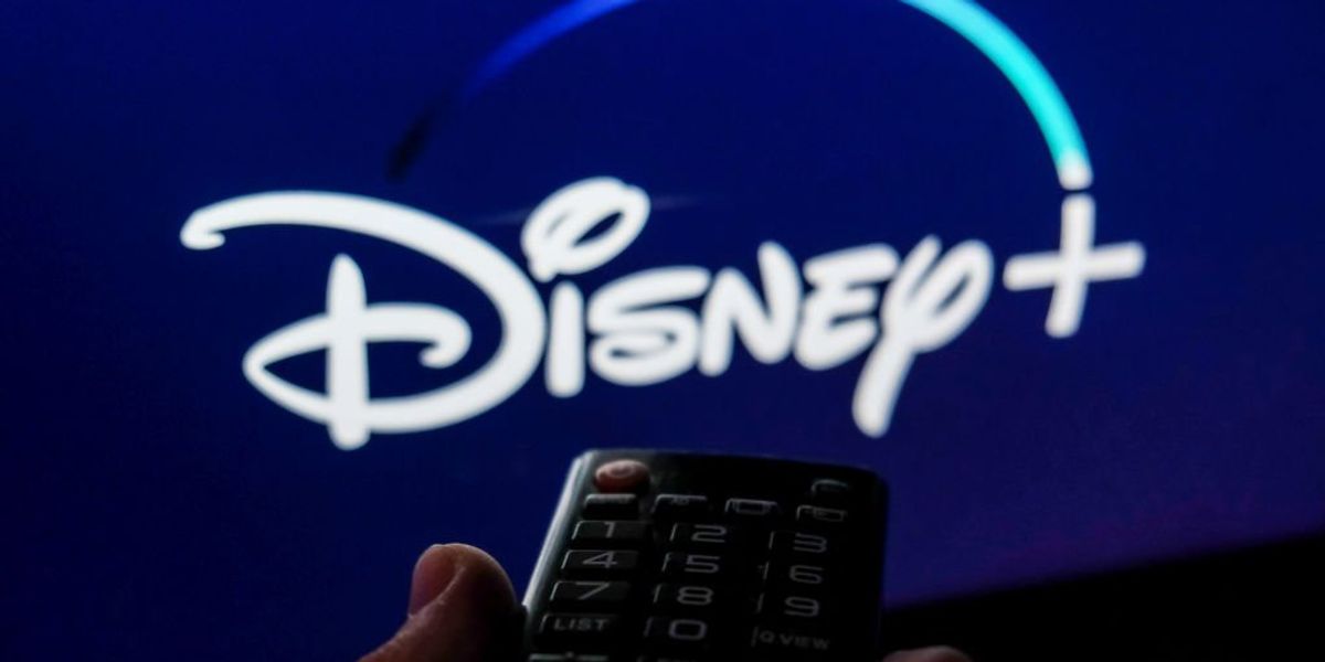 Távirányítót tartó kéz, előtte Disney+ logó a képernyőn