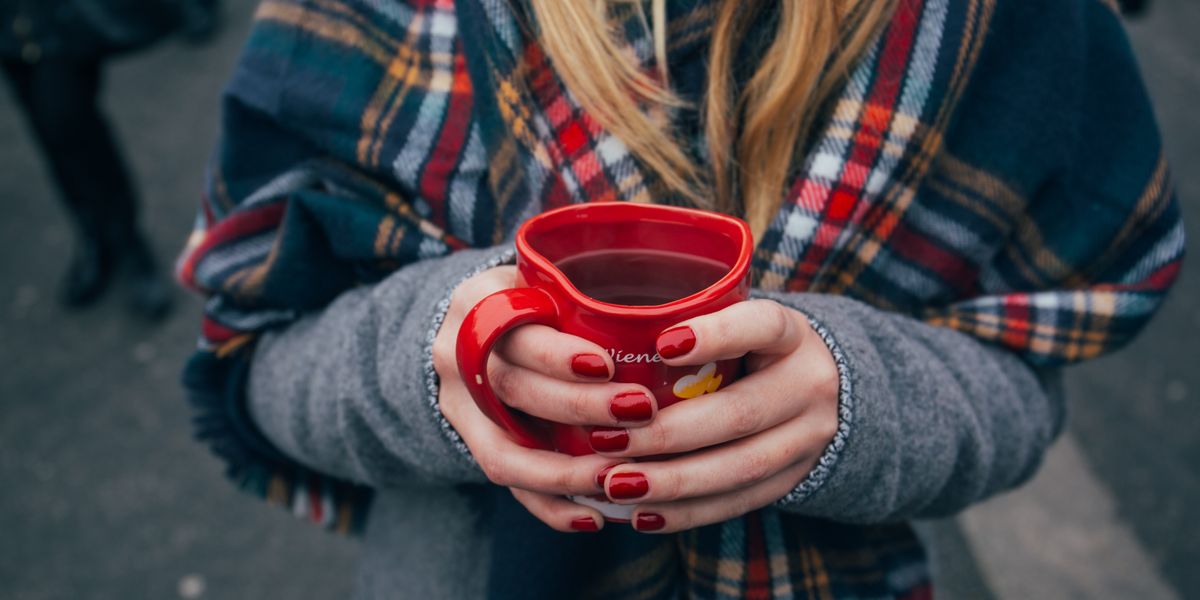 egy lány piros körmökkel fogja a teával töltött bögrét sálba burkolózva