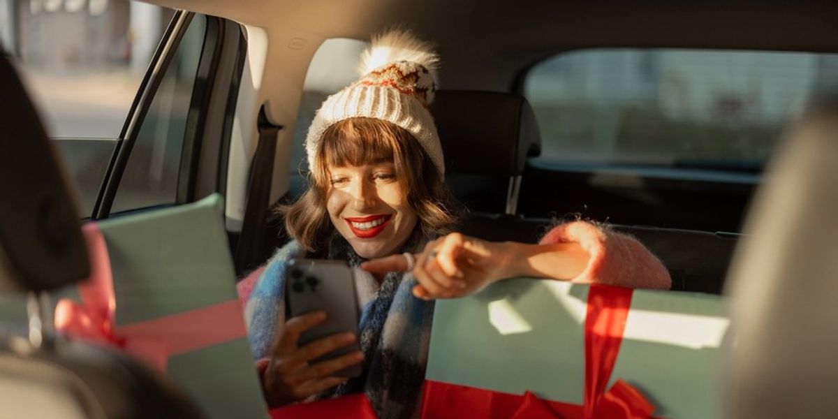 egy nő mosolyogva ül az autóban ajándékok mellett