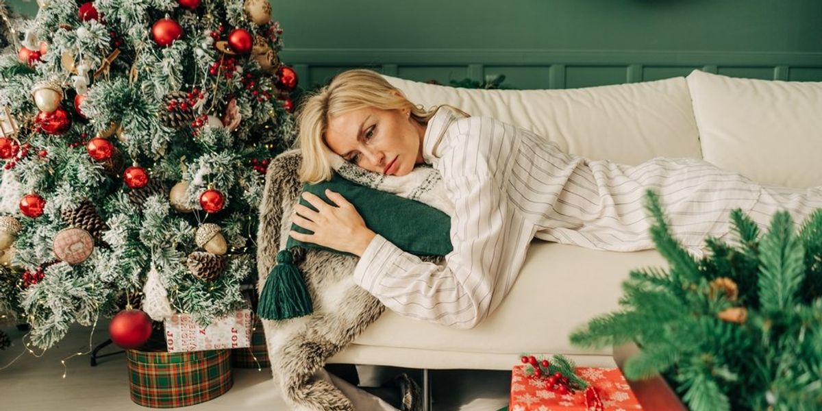 Fáradt nő fekszik a kanapén, mellette karácsonyfa és ajándékok