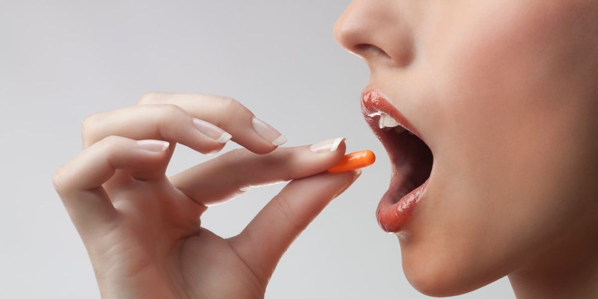C-vitamint a szájába tévő nő, másik kezében félbevágott narancs, benne vitaminok