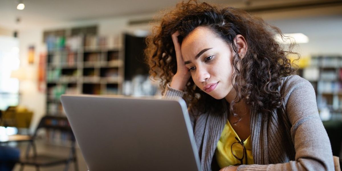 egy fiatal nő fogja a fejét a laptopja előtt