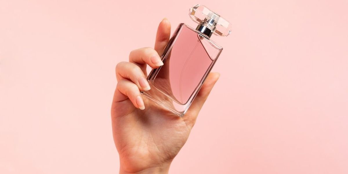 Parfümös üveget tartó női kéz rózsaszínű háttér előtt