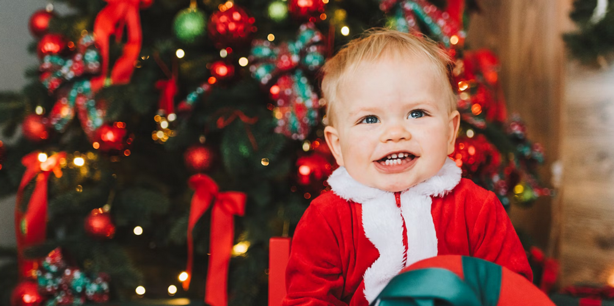 Csecsemő karácsonyi ajándékot tart a kezében egy karácsonyfa előtt