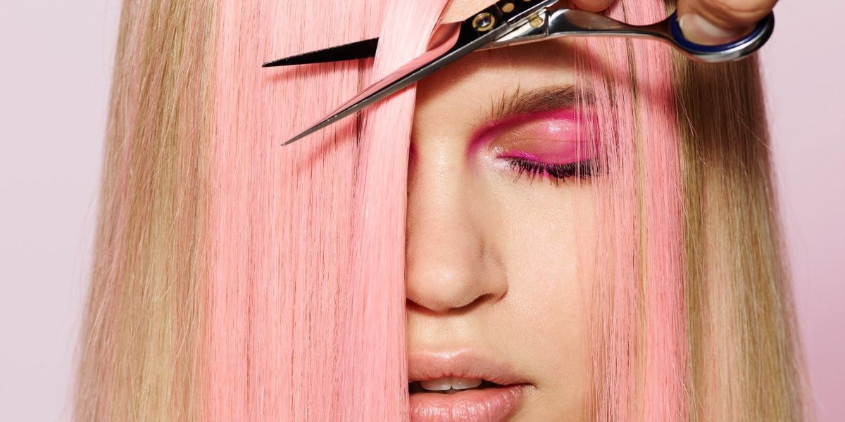 egy szőke-rózsaszín hajú nőnek vágják a haját elől egy ollóval