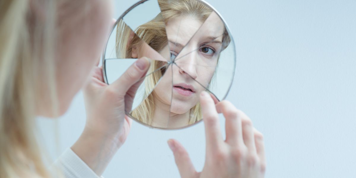 egy nő nézi magát a széttört tükörben