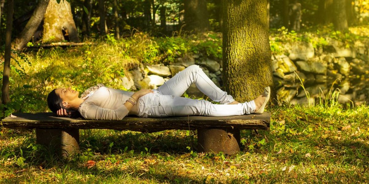 Fiatal nő csukott szemmel pihen egy padon a természetben