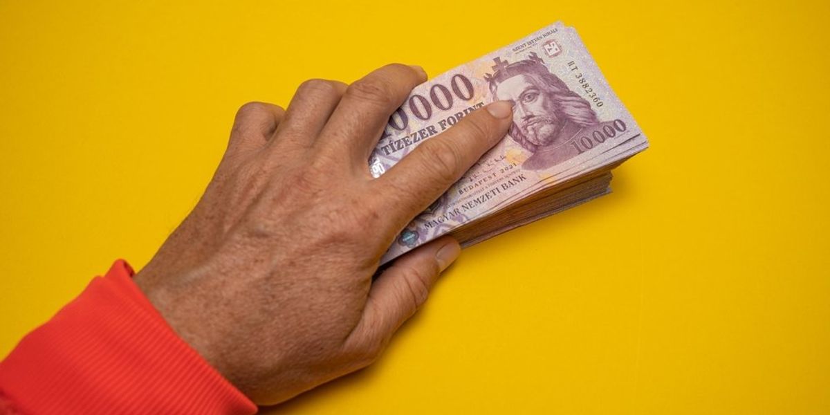 Forintköteget tartó kéz sárga háttéren