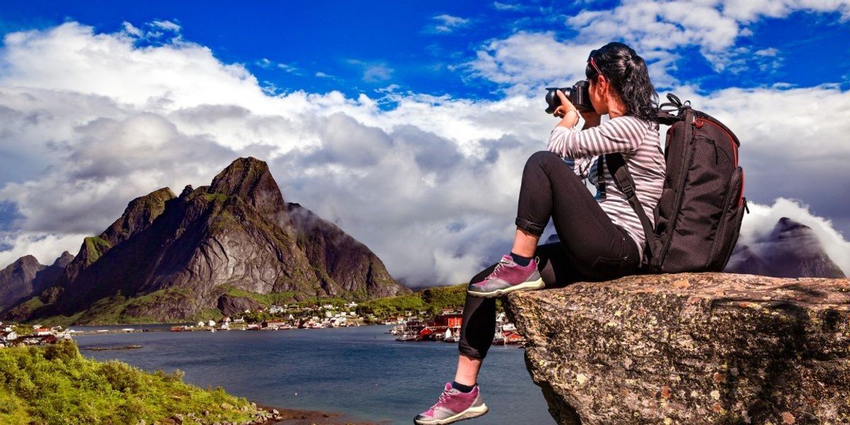 Fiatal nő a hegyen ülve fotóz hátizsákkal