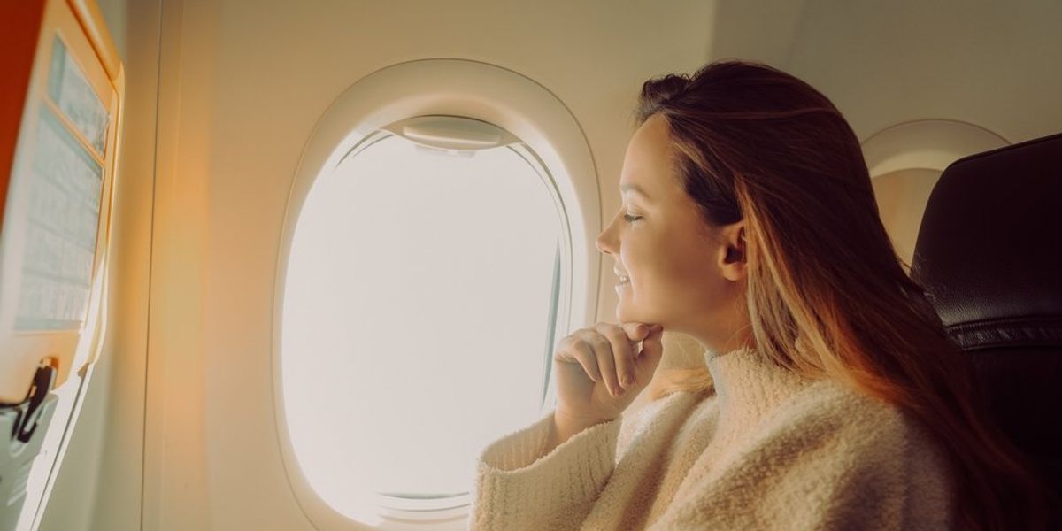 egy nő ül a repülőn mosolyogva az ablak mellett
