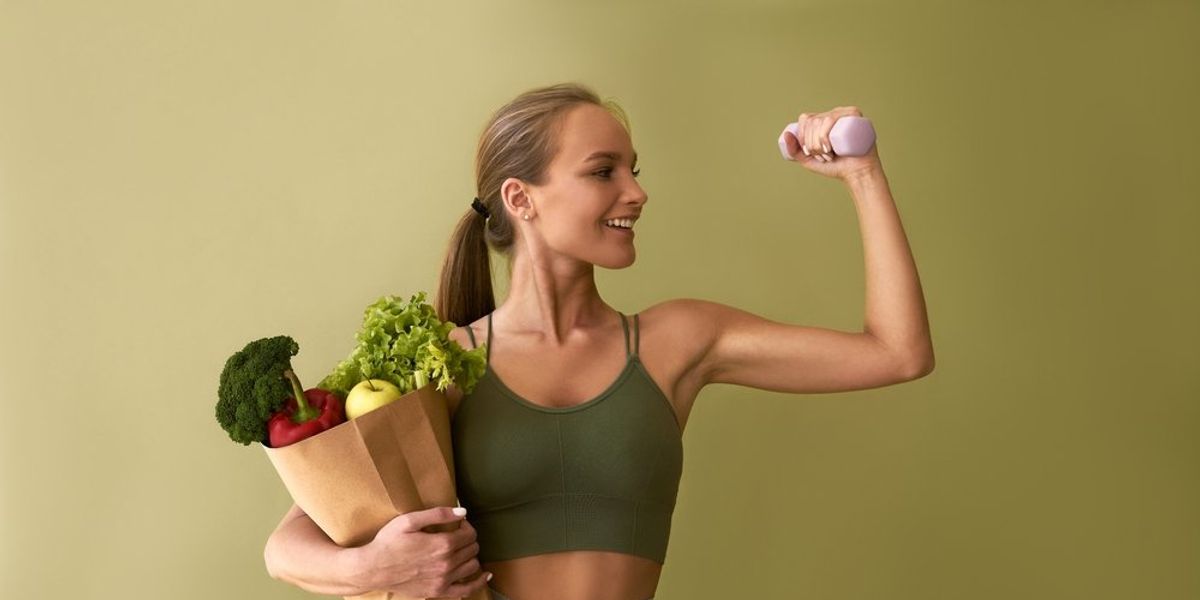 egy nő egyik kezében egy zacskó zöldség, másikban egy súlyzó