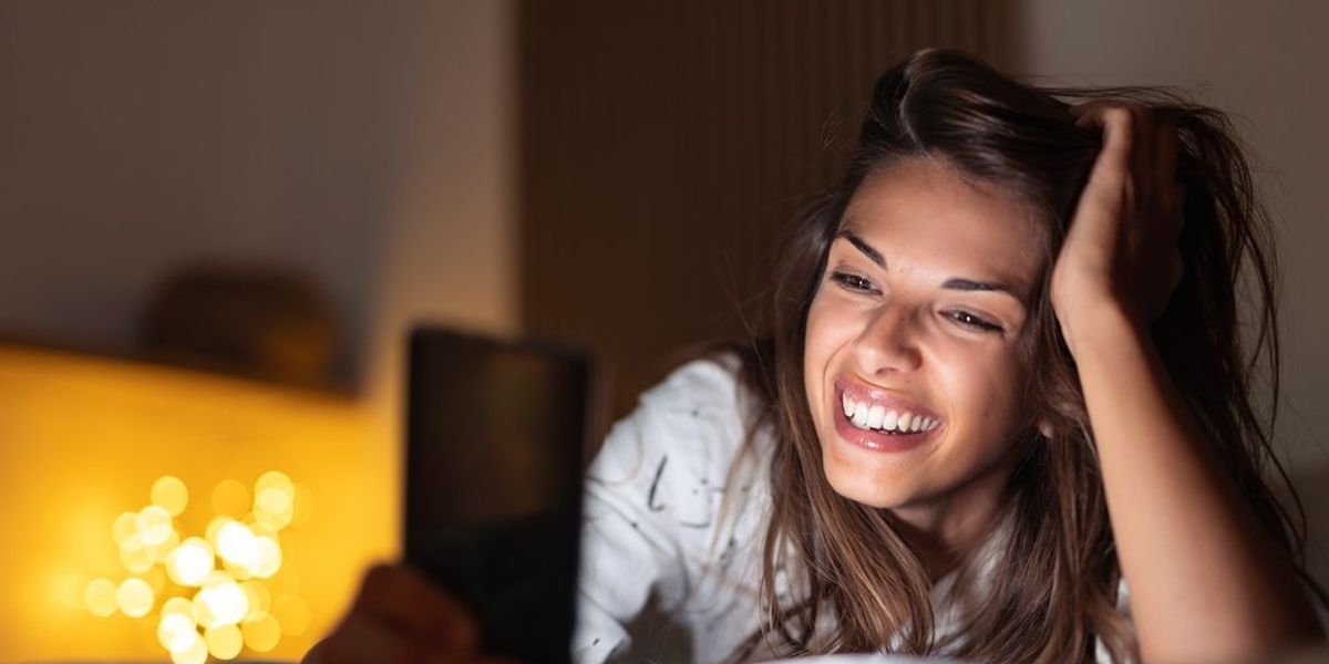 egy nő nevetve nézi a telefonját az ágyban