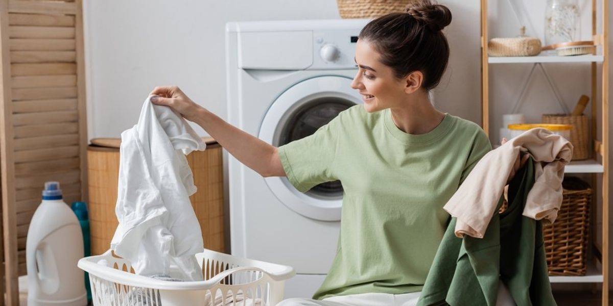 A mosógép előtt ruhákat válogató nő