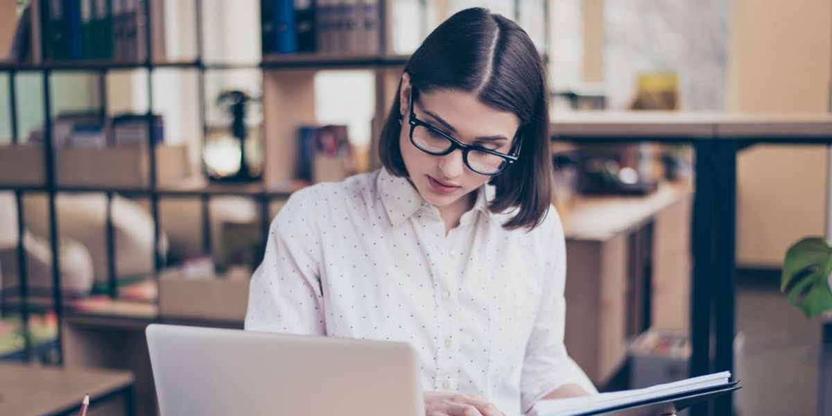 egy szemüveges nő a laptopja előtt ülve dolgozik