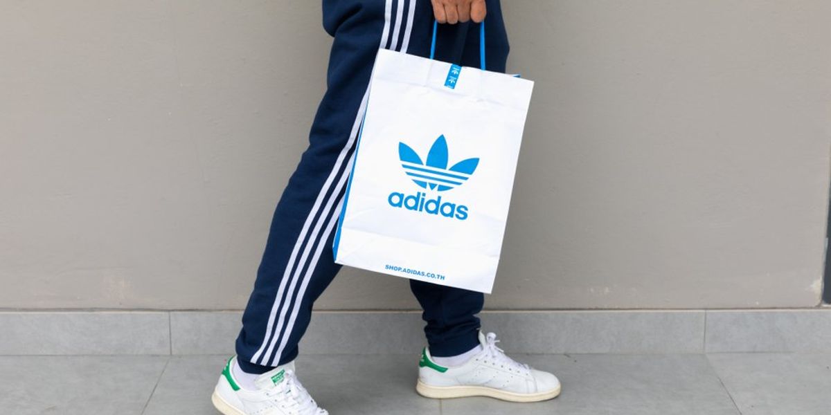 Adidas logóval ellátott zacskót tartó férfi kéz