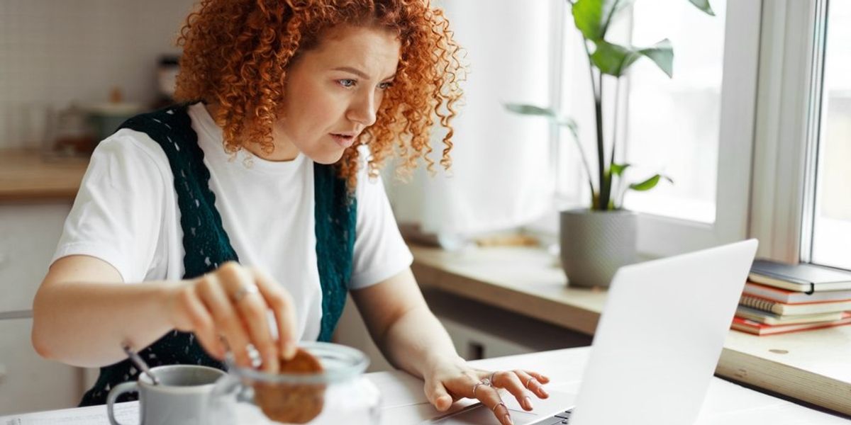 Vörös hajú nő munka közben kekszet eszik és kávét iszik