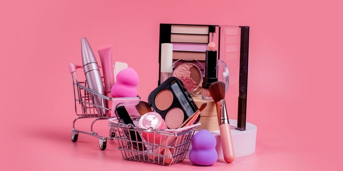 Kozmetikumok mini bevásárlókocsiban és kosárban, rózsaszín háttér előtt