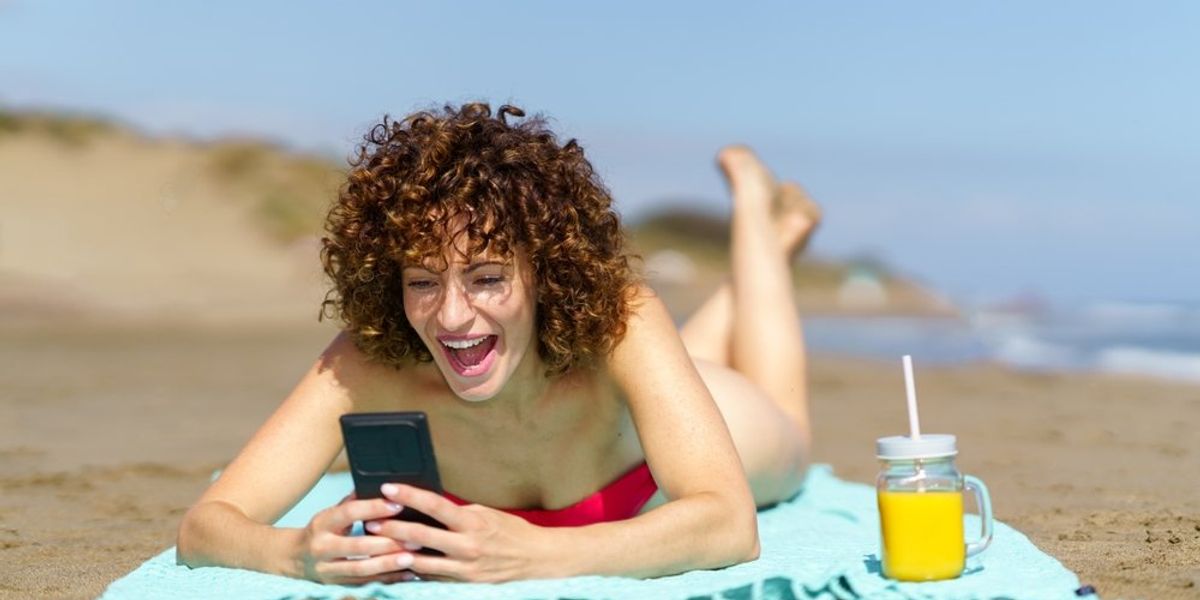 egy nő a telefonját nézi a tengerparton fekve