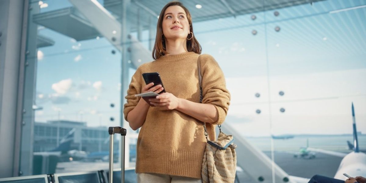 egy nő áll a reptéren a telefonjával a kezében