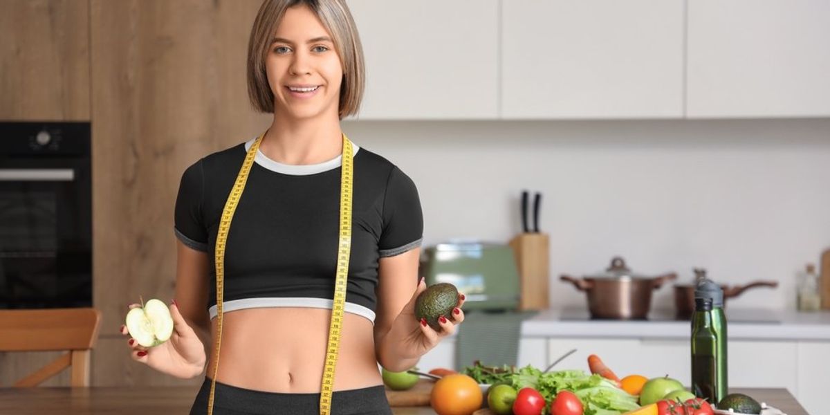 Almát és avokádót mutató sportos nő, mérőszalaggal a nyakában