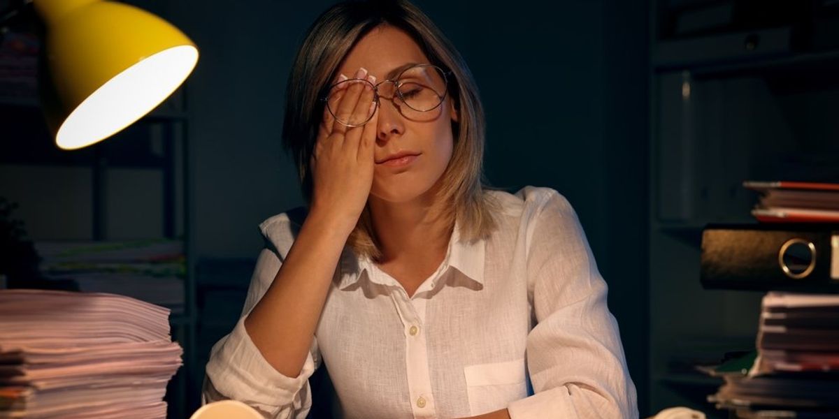 egy fáradt nő éjszaka ül az íróasztalánál és törölgeti a szemét, előtte kávéspoharak