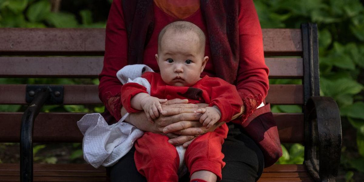 Egy nő karjában tartja gyermekét Pekingben