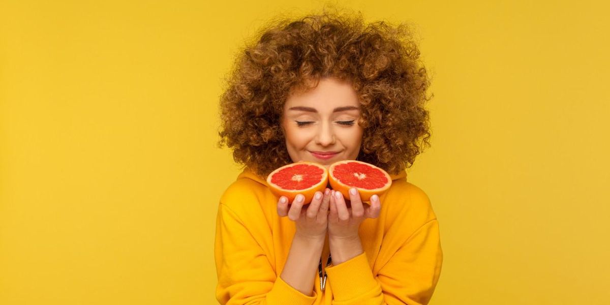 Boldog nő félbevágott grapefruitot szagol