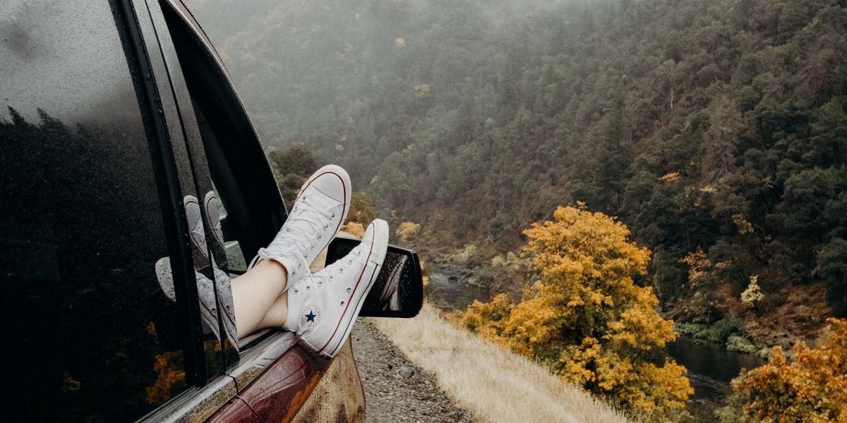 person's feet wearing white Converse sneakers on car door