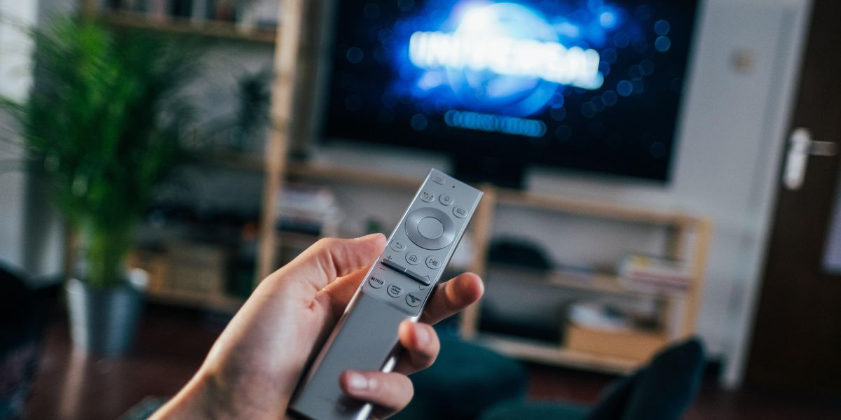 Egy ember a televízió távirányítóját fogja a kezében