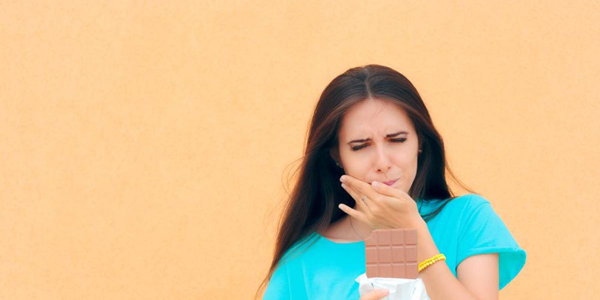 woman having toothache while eating chocolate