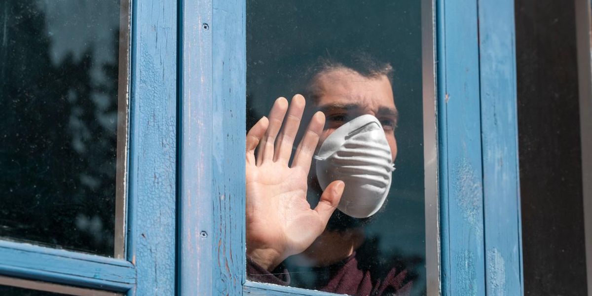 Maszkot viselő férfi a külvilágtól izoláltan áll az ablak előtt