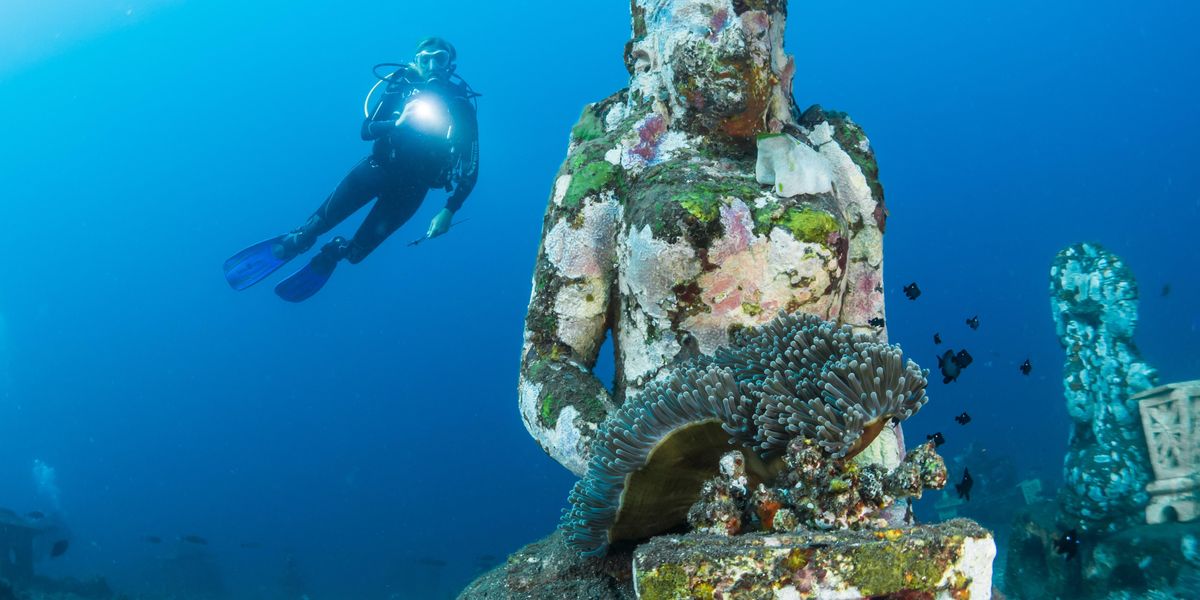 Egy búvár egy víz alatti szobrot figyel meg
