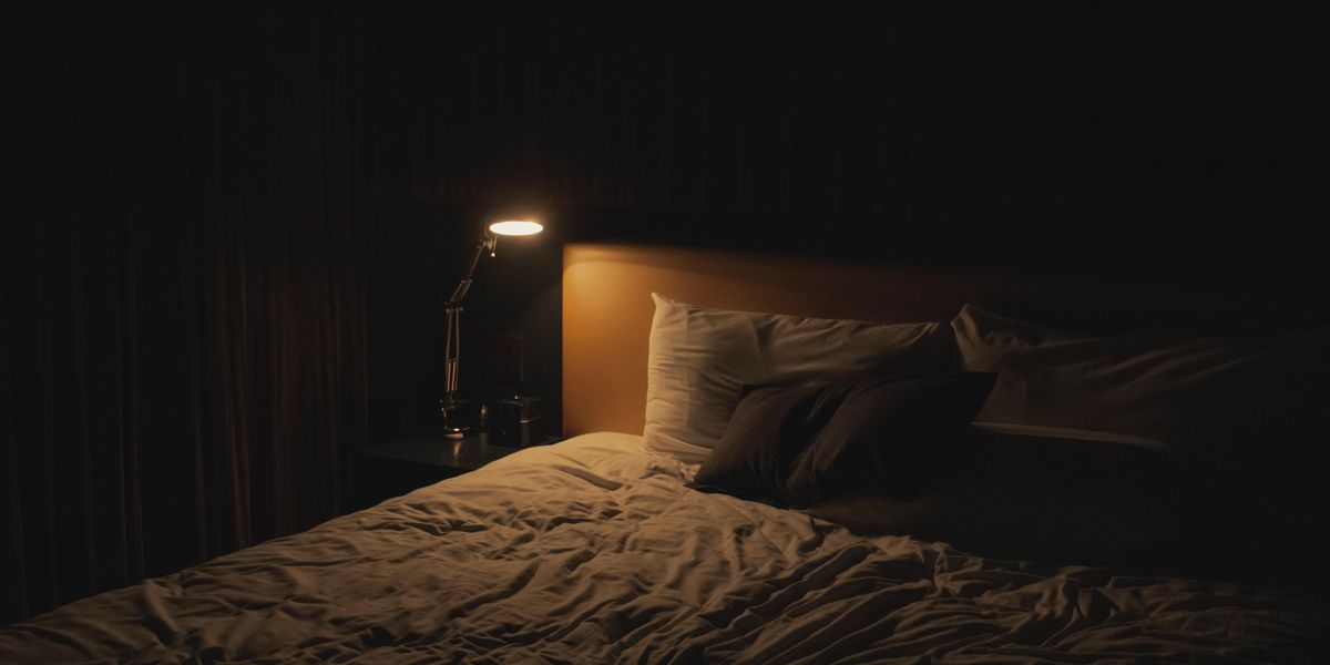 Egy éjjeli lámpa világít az ágy mellett