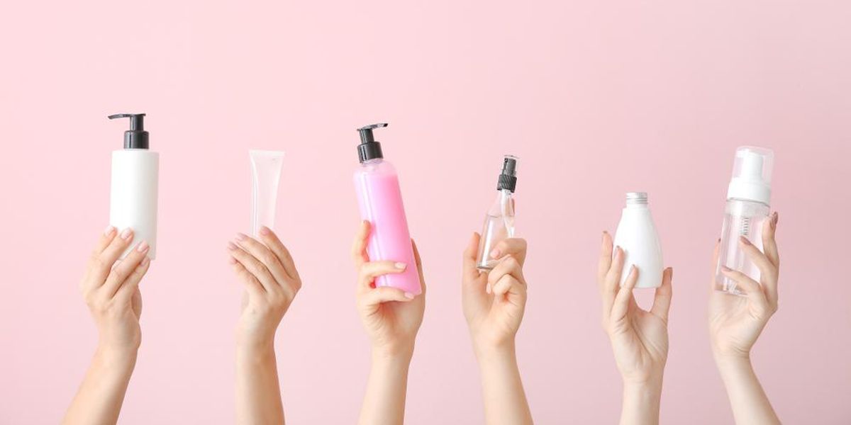 Különböző kozmetikai termékekeket tartó női kezek, rózsaszín háttér előtt