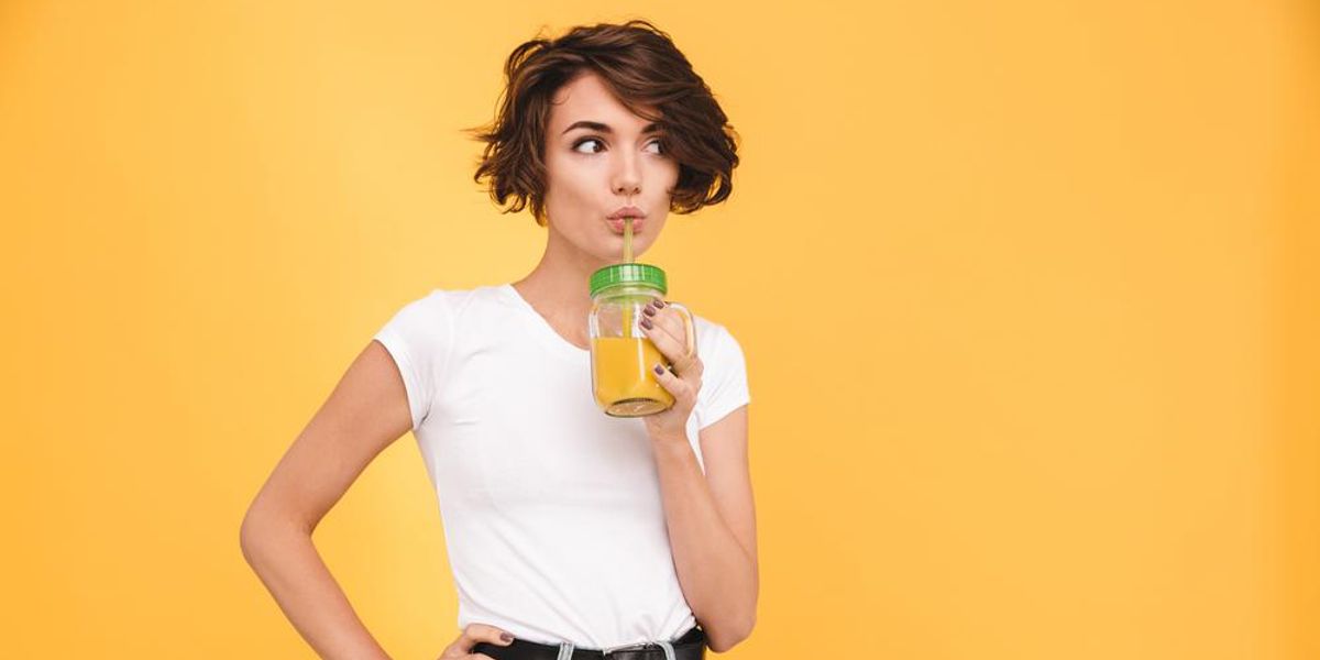 Fiatal nő narancslevet iszik egy pohárból, narancssárga háttér előtt