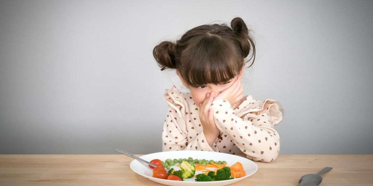 Egy gyerek az asztalnál ülve nem akar zöldséget enni